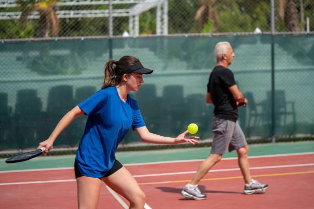 Woman playing a game with a lightweight pickleball paddle on an outdoor court with a partner in the background