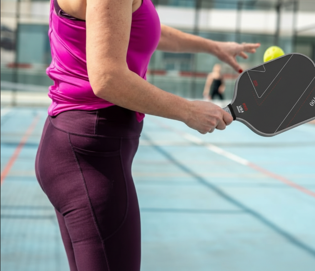 Side profile of a female player holding a black T700 pickleball paddle ready to serve on an outdoor court
