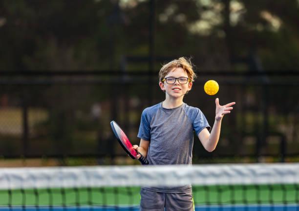 Young player wearing safety glasses practicing hand-eye coordination with a youth-sized pickleball paddle at the net.