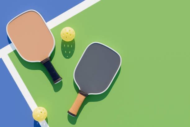 Top-down view of a beige composite and a grey pickleball paddle on a green and blue court surface
