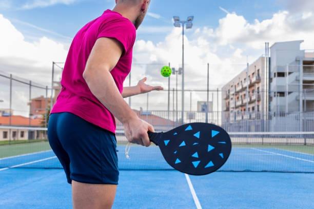 Male player in a pink shirt using a custom design black and blue pickleball paddle during an outdoor game