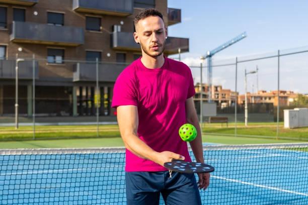 Player preparing to execute an underhand serve, holding the ball and a vibrant pickleball paddle, illustrating the basic serving mechanics.