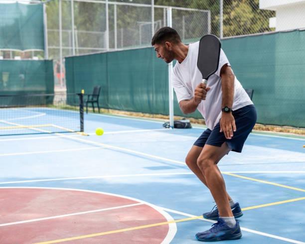 Beginner male player in a defensive stance, showcasing a proper continental grip on the pickleball paddle handle while tracking the ball.