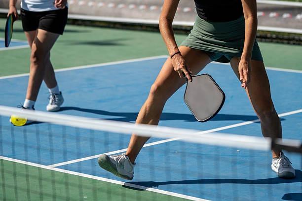 Female player demonstrating the proper athletic ready position at the non-volley zone line, holding her pickleball paddle centered and ready to react.