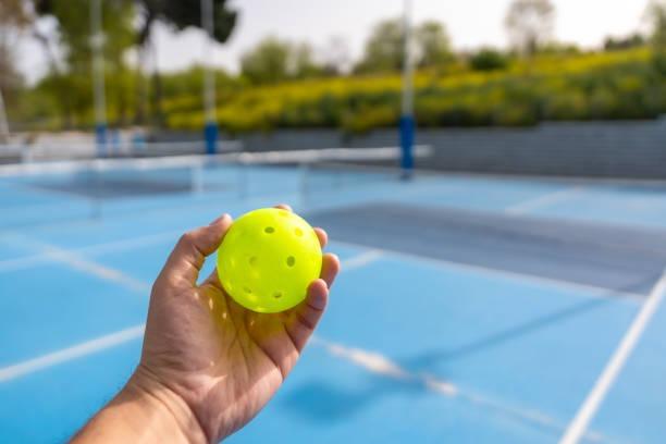Close-up of a high-visibility outdoor pickleball in a player's hand, an essential accessory to pair with quality pickleball paddles for a complete starter set.