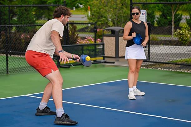 Mixed doubles team communicating on the court, holding their pickleball paddles in anticipation of the opponent's return shot.