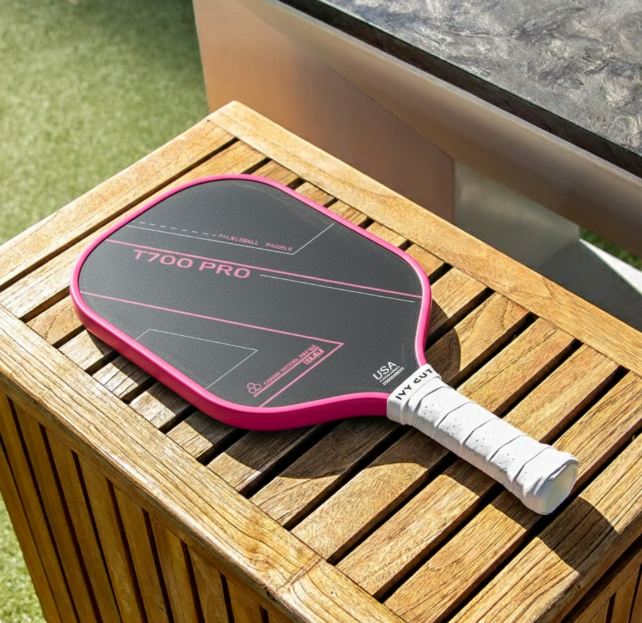 Pink and black T700 Pro carbon fiber pickleball paddle with a white grip resting on a wooden table