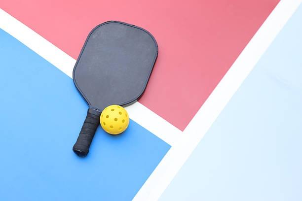 Top-down view of a graphite pickleball paddle on a contrasting red and blue court
