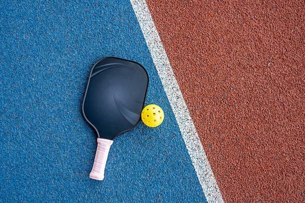 Close-up of a black pickleball paddle on a textured red and blue court surface
