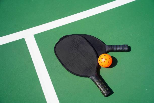 Pair of carbon fiber pickleball paddles on a green court with an orange high-visibility ball