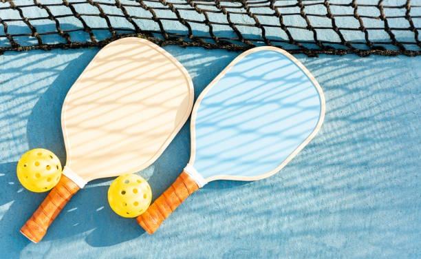 Sunlight casting net shadows on two lightweight pickleball paddles on a blue court