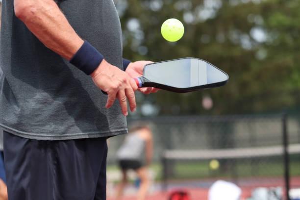 Player testing the static weight and balance point of a black edgeless pickleball paddle with a yellow ball