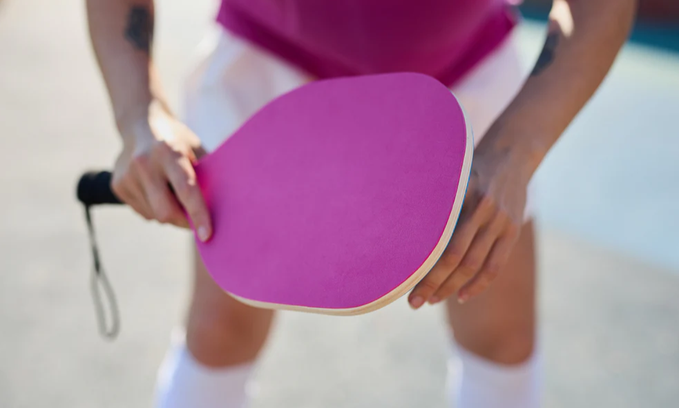 Person holding a vibrant pink pickleball paddle, ready for play on court.