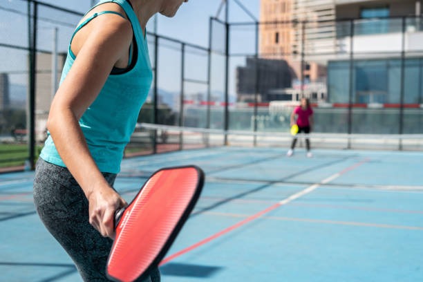 Woman holding a red pickleball paddle, ready to play on a bright blue court.