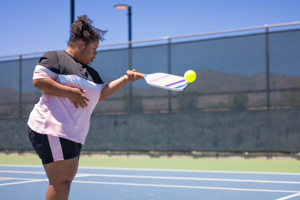 Person hitting a ball with a colorful pickleball paddle on a sunny court.