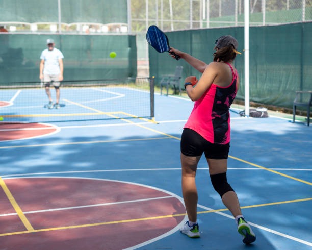 Woman playing pickleball with pickleball paddles, hitting the ball.