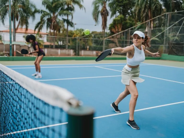 Woman playing pickleball, swinging a black paddle on a blue court. Many use pickleball paddles.